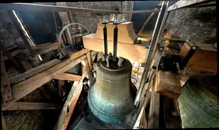 Nahaufnahme einer großen bronzenen Kirchenglocke und der hölzernen Turmkonstruktion.
