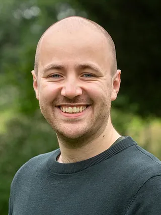 Porträt eines lächelnden, glatzköpfigen Mannes mit blauen Augen, trägt dunklen Pullover.