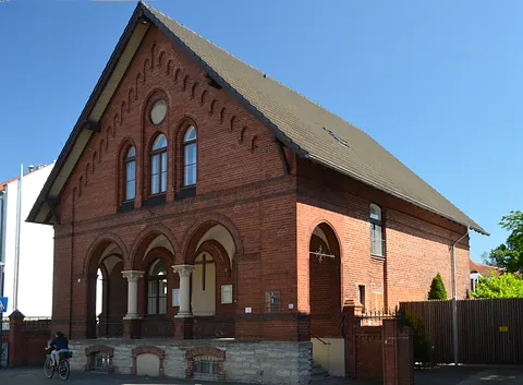 Moderne Backsteinkirche mit braunem Turm und violettem Banner über Freiheit.