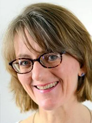Kopfaufnahme einer lächelnden Frau mit mittellangem braunem Haar und Brille in Schildpattoptik.