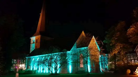Kirchengebäude nachts von hellen türkisfarbenen Scheinwerfern beleuchtet.