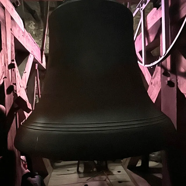 Massive Kirchenglocke mit rosa Licht beleuchtet, im hölzernen Glockenturmgerüst.