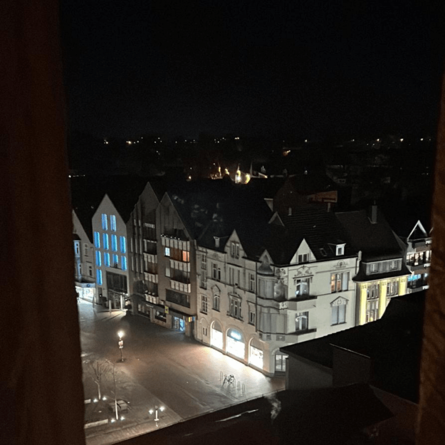 Nachtaufnahme eines leeren Stadtplatzes umgeben von beleuchteten historischen Gebäuden.