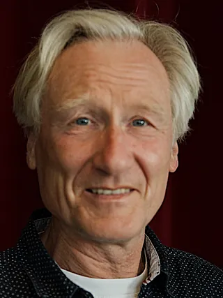 Portrait of a smiling man with blonde hair and a gray polo shirt.