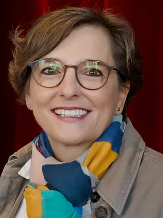 Porträt einer lächelnden Frau in Jeansjacke und rosa-blau gemustertem Schal.
