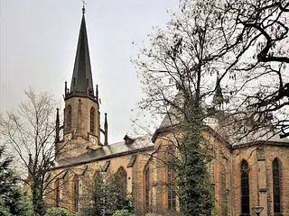 Neugotische Steinkirche mit hohem Turm und Bogenfenstern bei trübem Wetter.