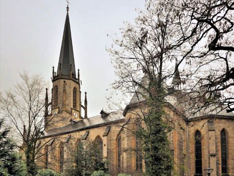 Neugotische Steinkirche mit hohem Turm und Bogenfenstern bei trübem Wetter.