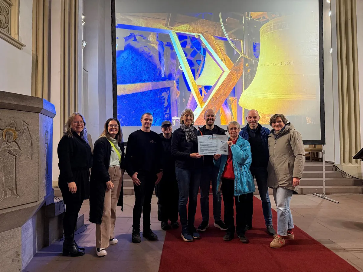 Gruppe hält UNESCO-Zertifikat in Kirche vor Projektion von Kirchenglocken.