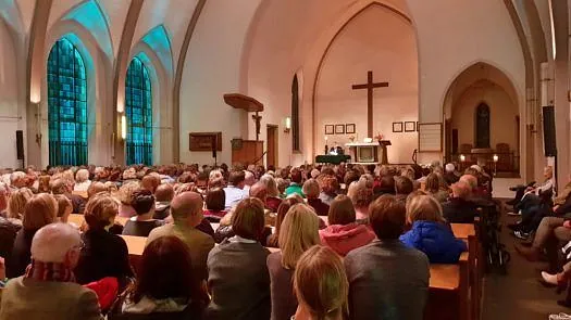 Kirchengemeinde versammelt sich zum Gottesdienst vor Altar und Holzkreuz.