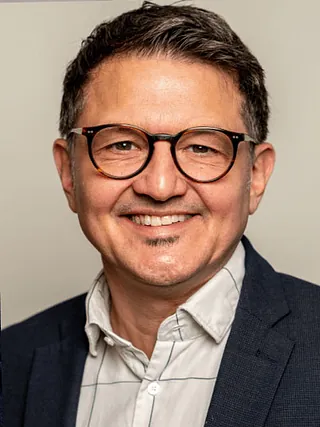 Professionelles Porträt eines lächelnden Mannes mit Brille in Schildpattoptik und Ziegenbart.