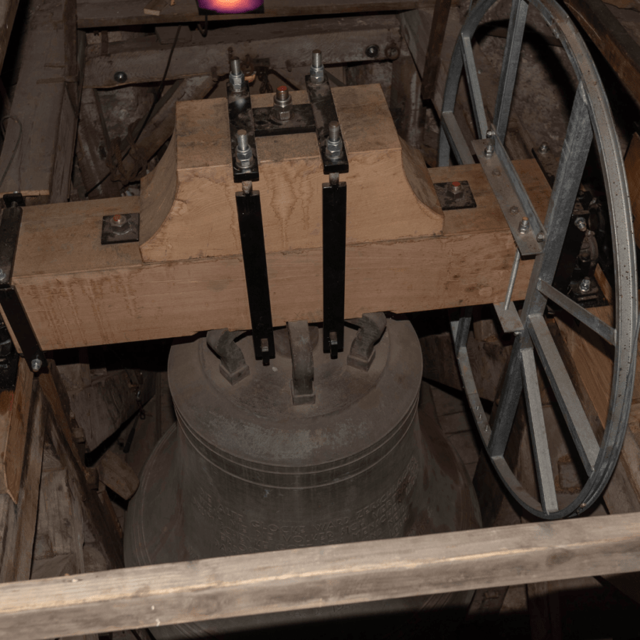 Nahaufnahme einer großen Kirchenglocke, befestigt an einem Holzbalken und Eisenrad.