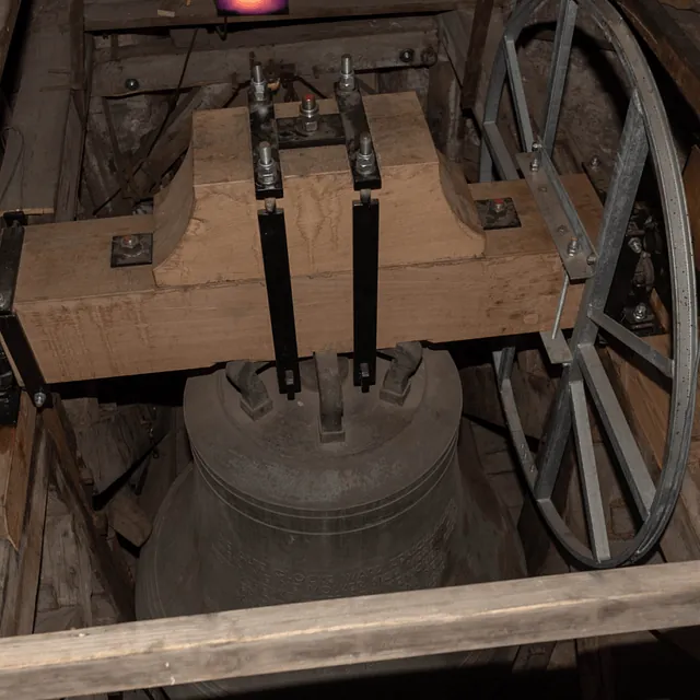 Nahaufnahme einer großen Kirchenglocke, befestigt an einem Holzbalken und Eisenrad.