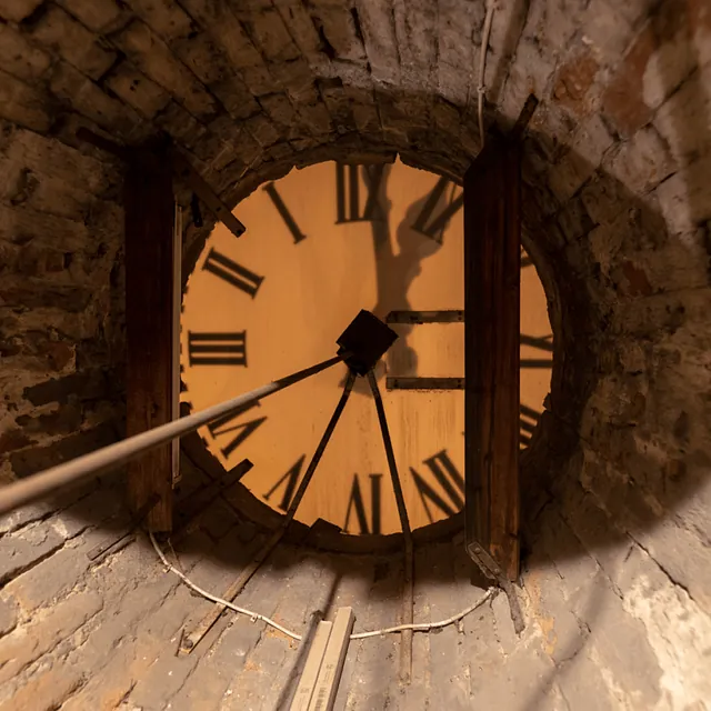Blick nach oben im Schacht des Ziegelturms auf das beleuchtete Zifferblatt der Uhr.