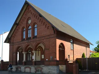 Weiße Kirche mit steilem Dach und kleinem Turm, umrahmt von kahlen Bäumen.