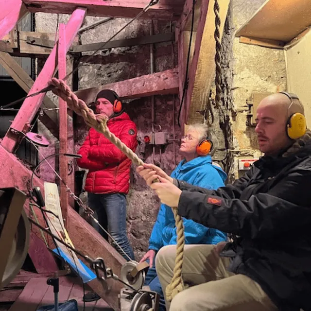 Drei Glockenläuter mit Gehörschutz ziehen an einem dicken Seil im Glockenturm.