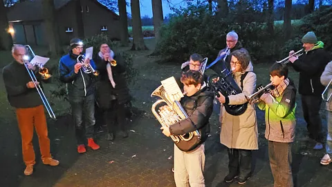 Kirchen-Blasorchester spielt, geleitet von einem Dirigenten, vor einem Holzkreuz.
