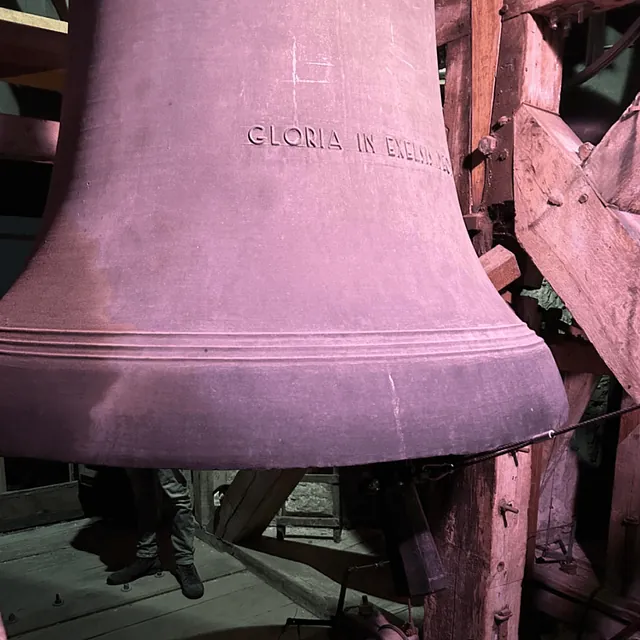 Nahaufnahme einer massiven Kirchenglocke mit der Aufschrift „GLORIA IN EXCELSIS“ im Turm.