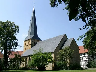 Historische Steinkirche mit hohem Schieferdach gegen blauen Himmel.