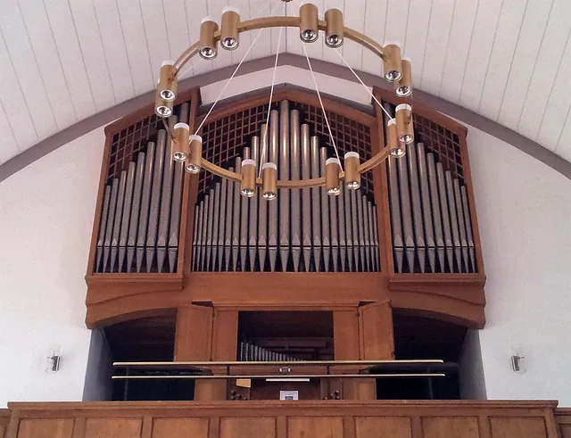 Kirchenorgel mit silbernen Pfeifen und großem, kreisförmigem Goldleuchter.
