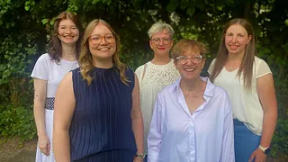 Kirchenchor singt unter Leitung des Dirigenten vor Buntglasfenster und Kreuz.