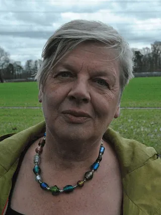 Porträt einer Frau mit kurzen grauen Haaren und bunter Glasperlenkette im Freien.