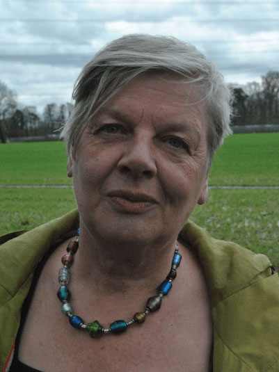 Porträt einer Frau mit kurzen grauen Haaren und bunter Glasperlenkette im Freien.
