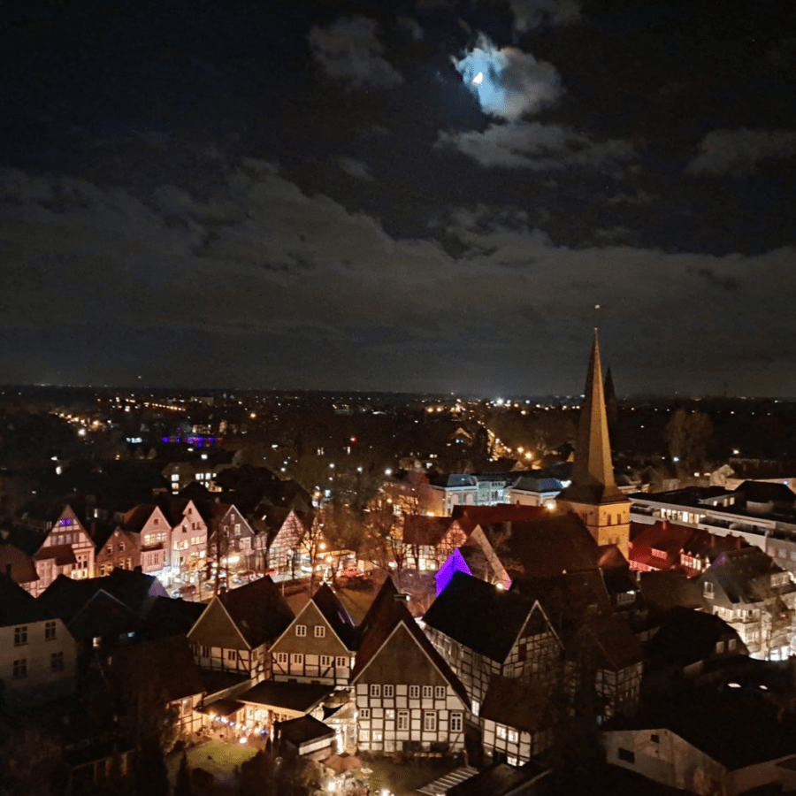 Nächtliche Luftaufnahme eines Stadtzentrums mit Fachwerkhäusern und Kirchturmspitze.