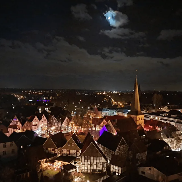 Nächtliche Luftaufnahme eines Stadtzentrums mit Fachwerkhäusern und Kirchturmspitze.