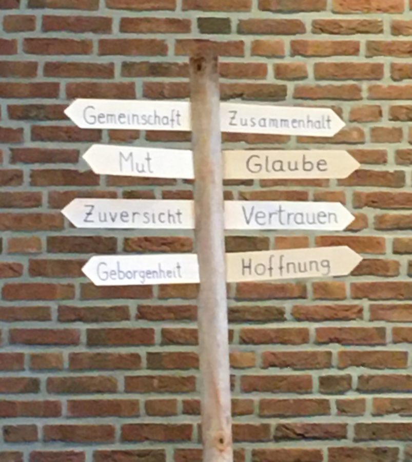 Wegweiser mit Werten wie Glaube, Hoffnung, Vertrauen, Gemeinschaft, Mut.