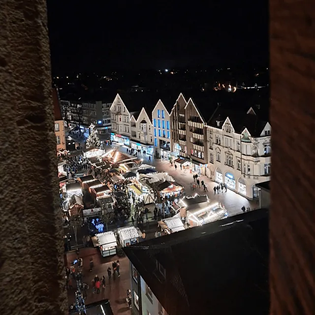 Nachtaufnahme eines Weihnachtsmarktes umgeben von beleuchteten historischen Gebäuden.