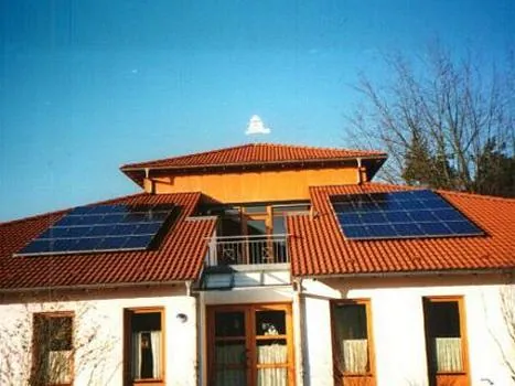 Kirchengebäude mit rotem Ziegeldach, Balkon und installierten Solarpaneelen.