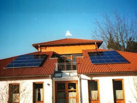 Kirchengebäude mit rotem Ziegeldach, Balkon und installierten Solarpaneelen.