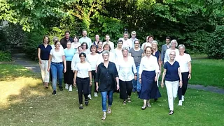 Kirchenchor singt unter Leitung des Dirigenten vor Buntglasfenster und Kreuz.