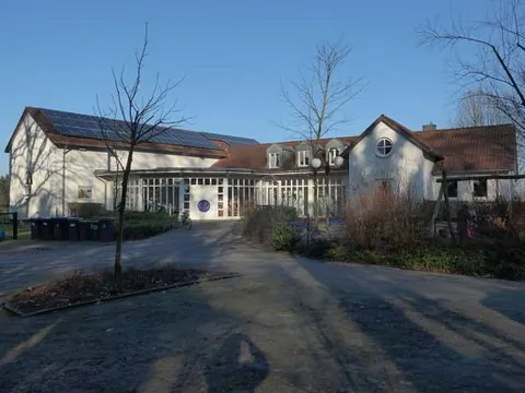 Weißes Gemeindezentrum mit Glasfassade und Solarpaneelen auf dem Dach.