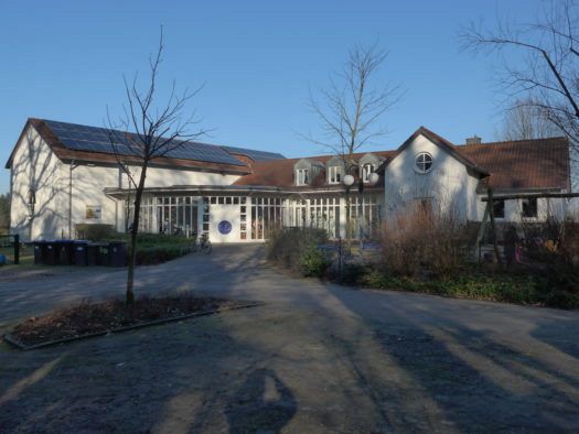 Weißes Gemeindezentrum mit Glasfassade und Solarpaneelen auf dem Dach.