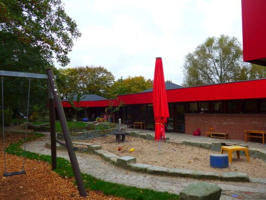 Außenbereich des Kirchen-Kindergartens mit Sandkasten und Schaukeln.